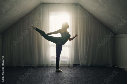 Woman doing yoga stretching exercises near big window at home