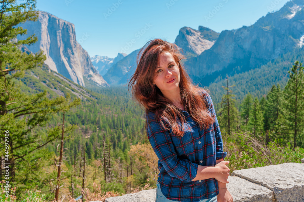 A cute young woman walks through a green valley in Yosemite National Park with a view of the mountains