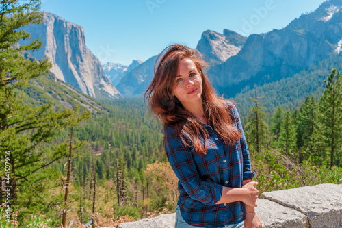 A cute young woman walks through a green valley in Yosemite National Park with a view of the mountains © KseniaJoyg