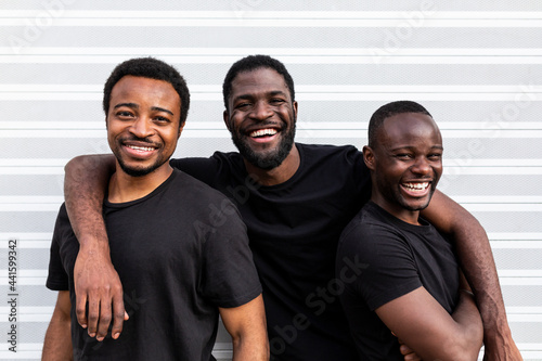 Cheerful black male friends embracing near striped wall