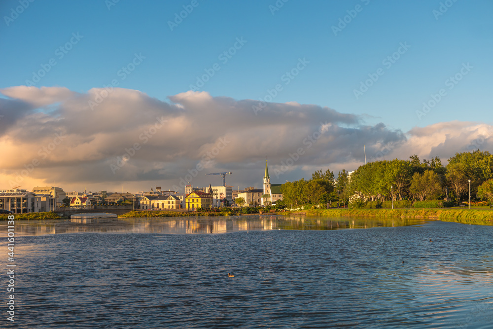 Beautiful view over historical downtown in Reykjavik at warm Summer sunset in the city lake Tjornin, and city park, Iceland.