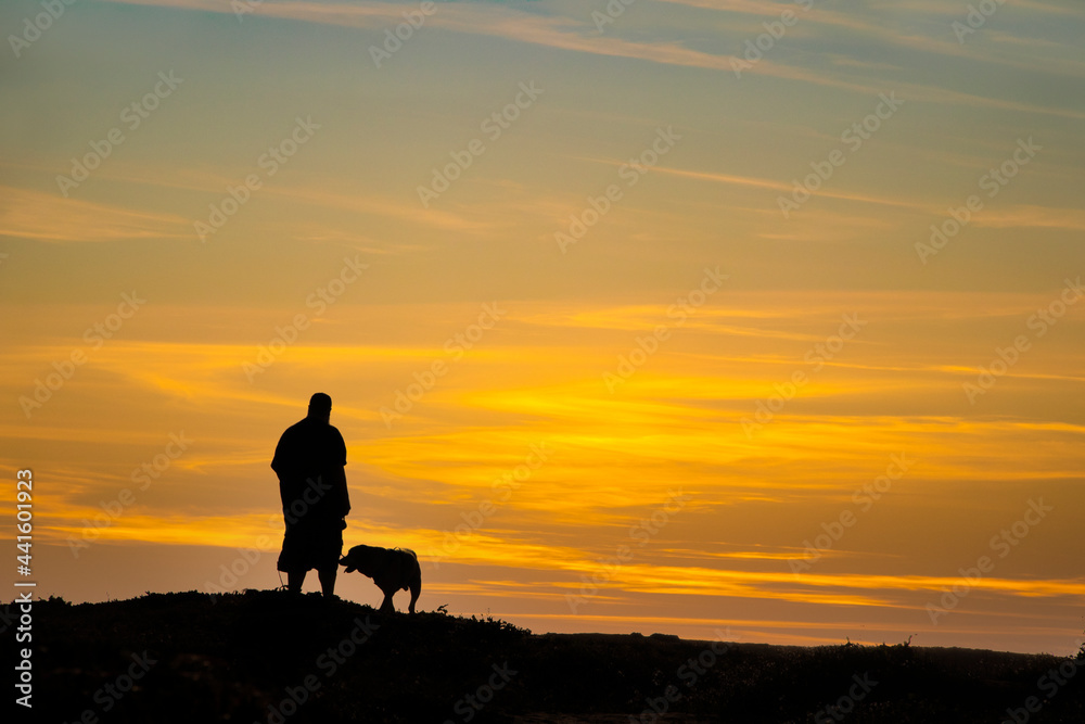 Black and white silhouette of man and his dog on top of hill at sunset -  room for text copy
