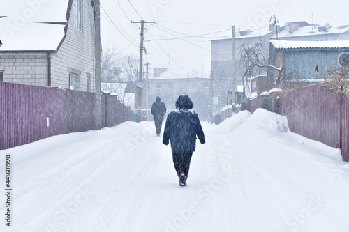 Heavy snow fell asleep on a rural road along which a woman is walking.