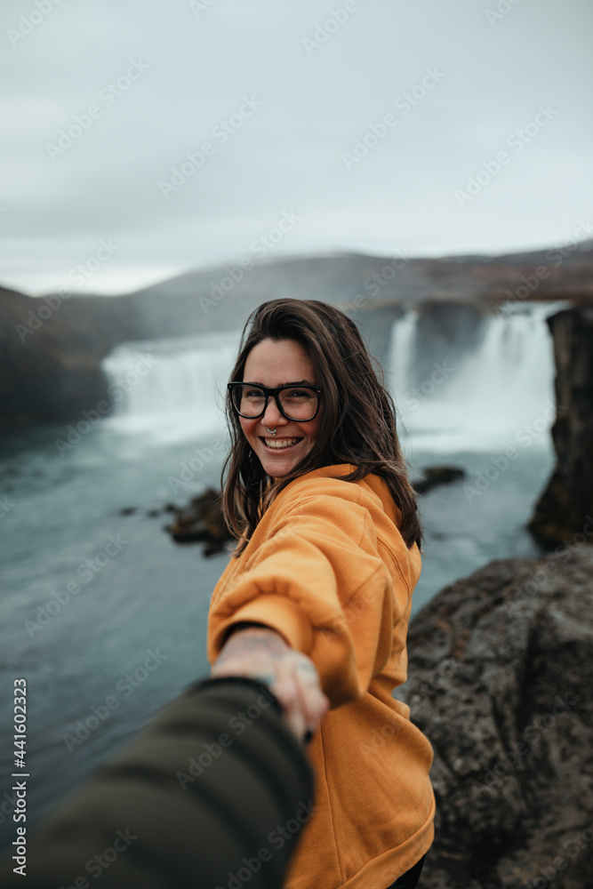 Smiling woman in eyeglasses holding hand of person near waterfall Smiling woman in eyeglasses holding hand of person near waterfall