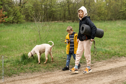 A mother and a young son walk in the park. A woman with a tourist mat and a boy walk about the road in the park, the forest.