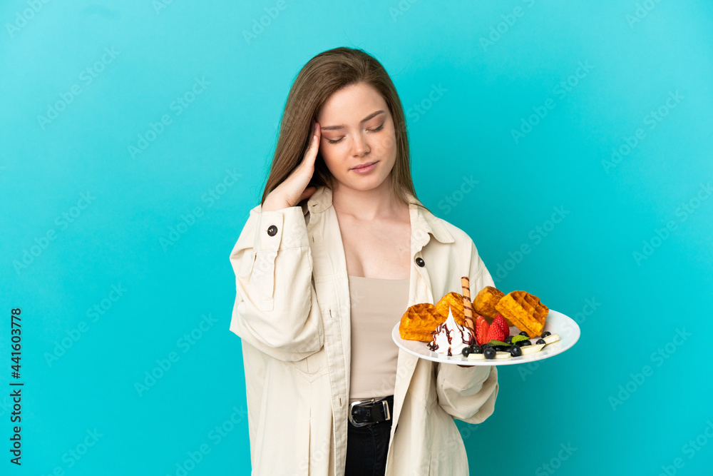 Teenager girl holding waffles over isolated blue background with headache