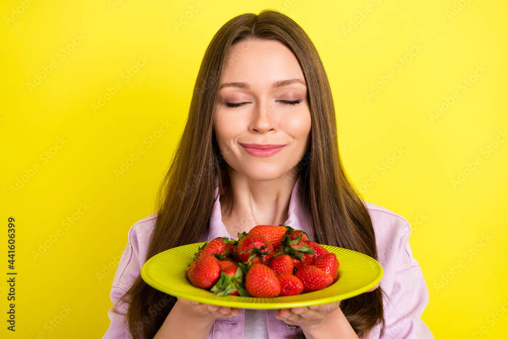 Portrait of attractive dreamy cheerful girl smelling strawberries isolated over bright yellow color background Portrait of attractive dreamy cheerful girl smelling strawberries isolated over bright yellow color background