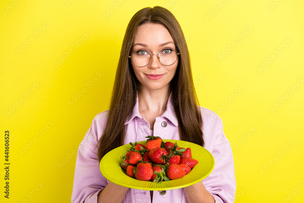 Photo portrait young woman in spectacles keeping plate with strawberries smiling isolated vibrant yellow color background Photo portrait young woman in spectacles keeping plate with strawberries smiling isolated vibrant yellow color background