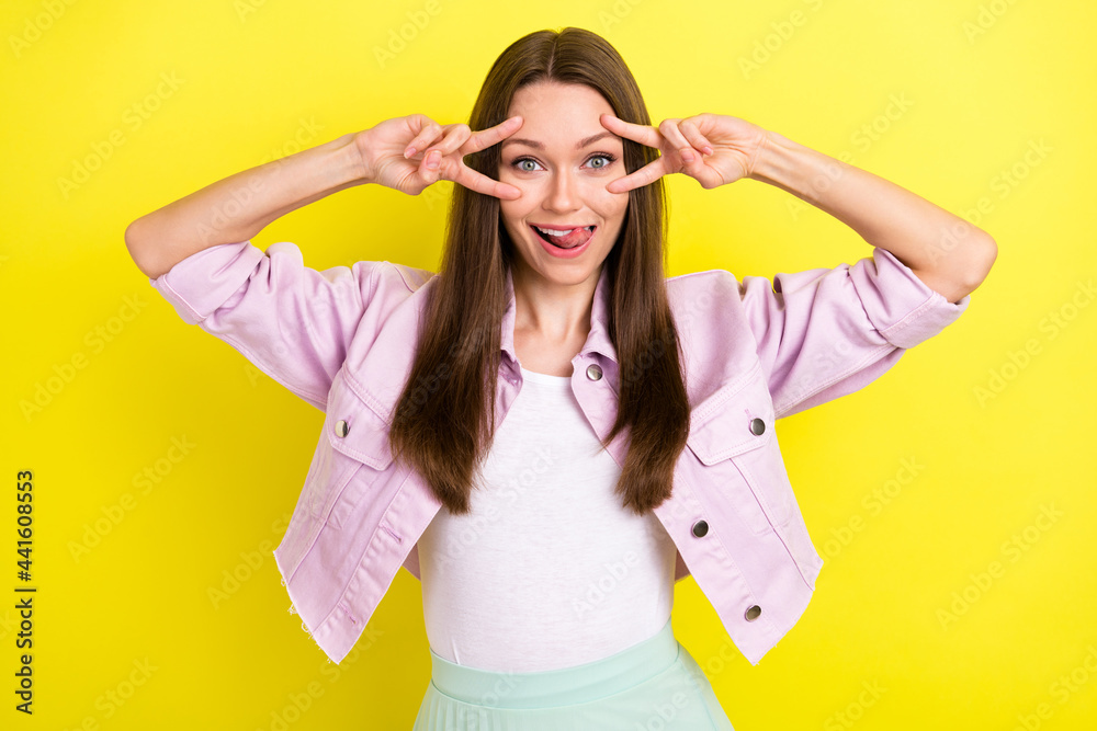 Photo portrait smiling girl showing v-sign gesture licking lips isolated bright yellow color background Photo portrait smiling girl showing v-sign gesture licking lips isolated bright yellow color background