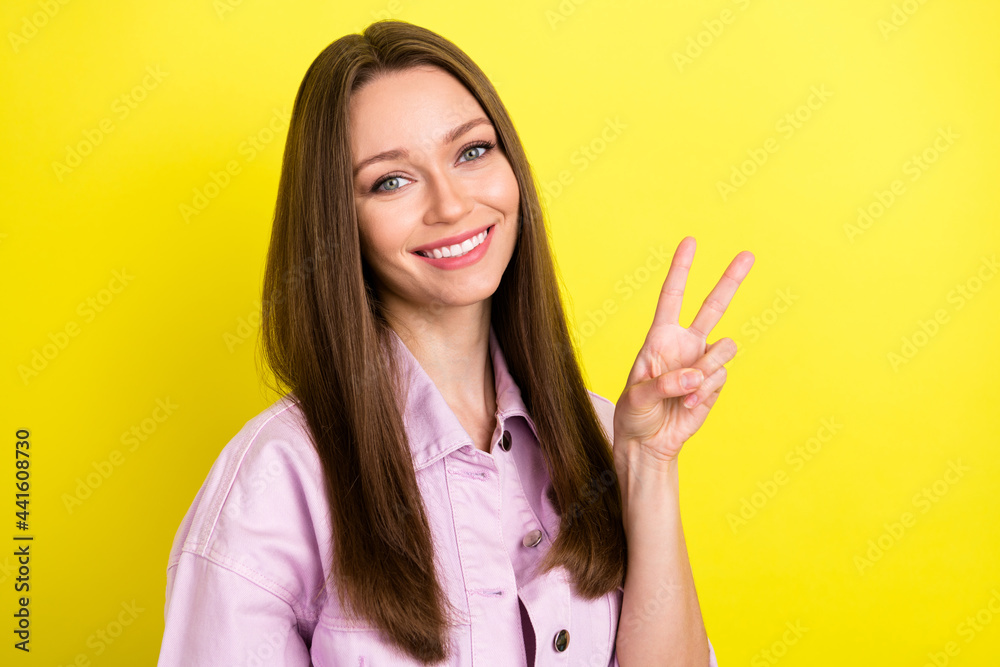 Portrait of attractive cheerful girl showing v-sign having fun rest isolated over bright yellow color background Portrait of attractive cheerful girl showing v-sign having fun rest isolated over bright yellow color background