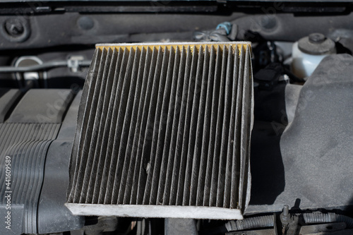 An old dirty cabin air filter under car hood for replacement. Car maintenance and air quality concept.