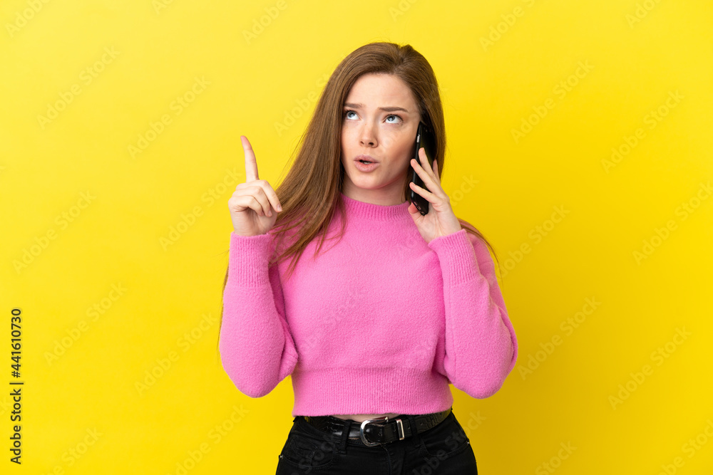 Teenager girl using mobile phone over isolated yellow background thinking an idea pointing the finger up Teenager girl using mobile phone over isolated yellow background thinking an idea pointing the finger up
