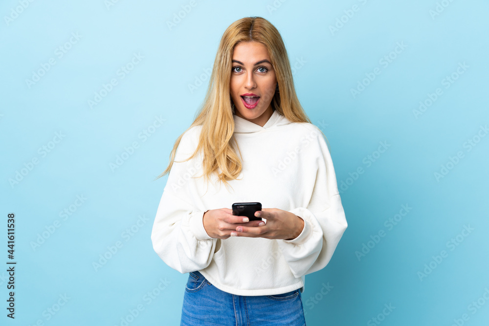 Young Uruguayan blonde woman over isolated blue background surprised and sending a message Young Uruguayan blonde woman over isolated blue background surprised and sending a message