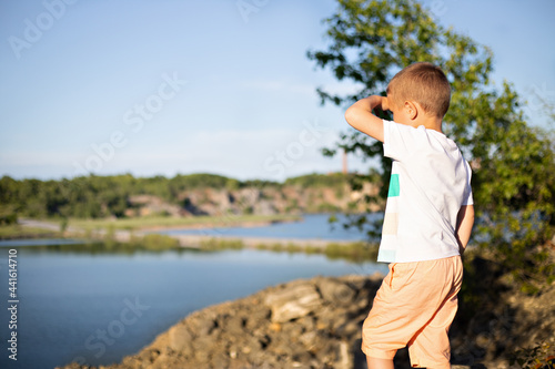 a little boy in a white t-shirt and orange shorts stands on the top of the mountain and looks at the lake