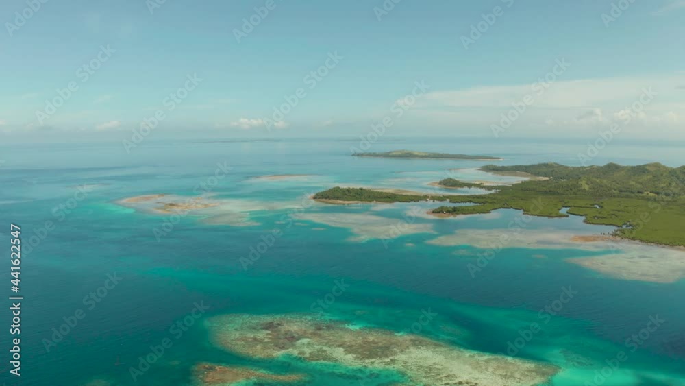 Coral atoll with blue water and a tropical island in the ocean on a sunny day. Bucas grande, Philippines. Summer and travel vacation concept. Coral atoll with blue water and a tropical island in the ocean on a sunny day. Bucas grande, Philippines. Summer and travel vacation concept.