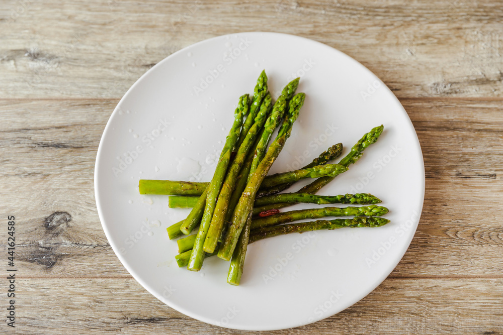 Cooked green asparagus in a white plate on a wooden table background.