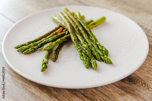 Cooked green asparagus in a white plate on a wooden table background.