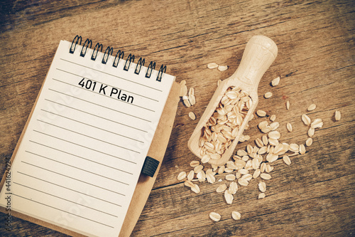 401 k Plan text on booknote with oats in spoon on wood table.