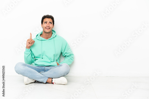 Caucasian handsome man sitting on the floor thinking an idea pointing the finger up