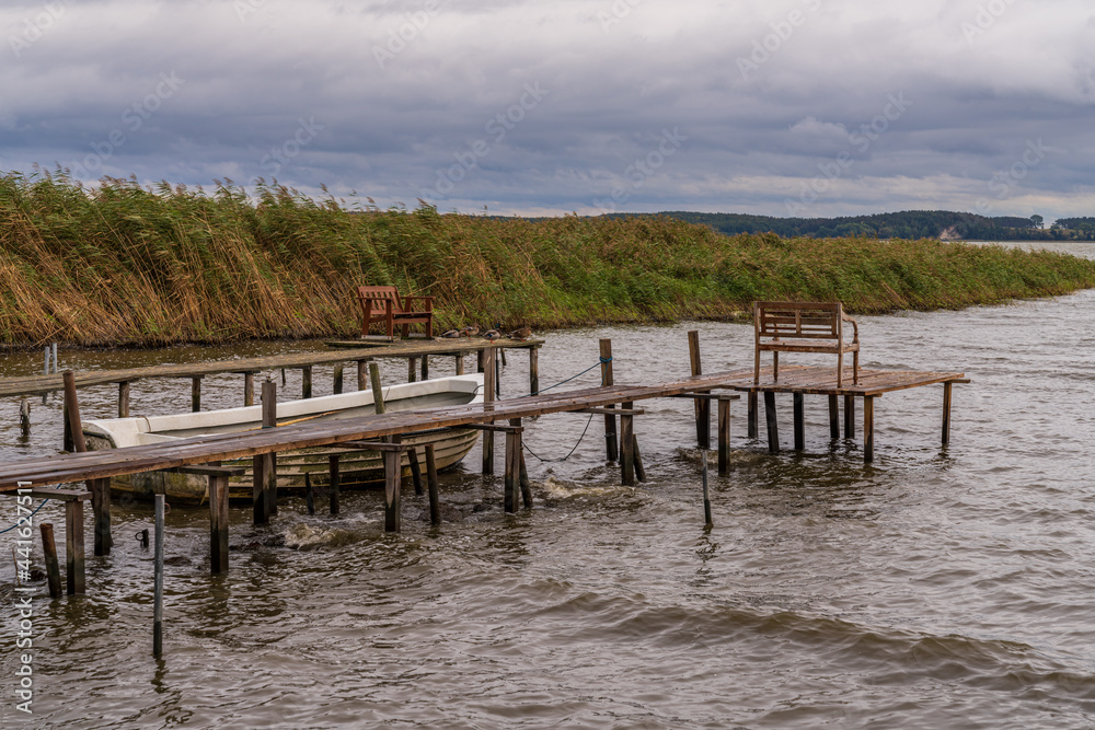 A wooden pier with a boat and some benches on the coast of the Krumminer Wiek in Neeberg, Mecklenburg-Western Pomerania, Germany A wooden pier with a boat and some benches on the coast of the Krumminer Wiek in Neeberg, Mecklenburg-Western Pomerania, Germany