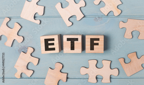 Blank puzzles and wooden cubes with the ETF Exchange Traded Funds lie on a light blue background.