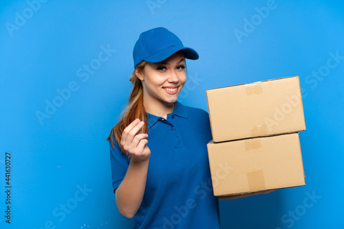 Delivery girl over isolated blue wall making money gesture