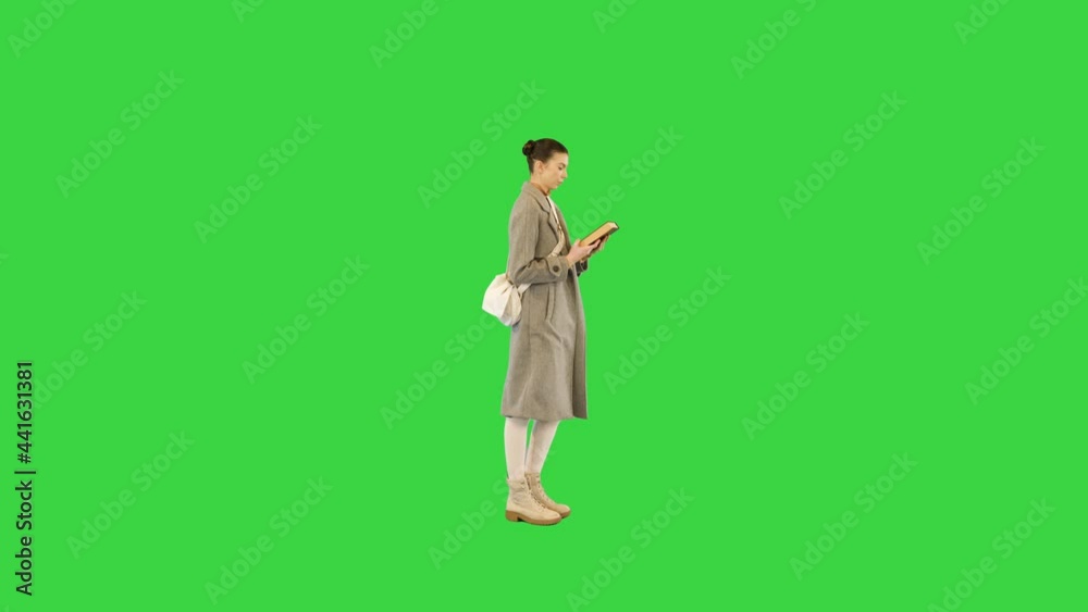 Young woman in stylish clothes walks with a book, stops and closes it on a Green Screen, Chroma Key. Young woman in stylish clothes walks with a book, stops and closes it on a Green Screen, Chroma Key.