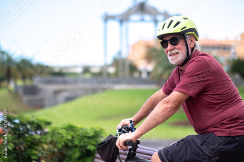 Youthful senior man in activity with bicycle in urban street. Attractive white-haired elderly retiree enjoying retirement