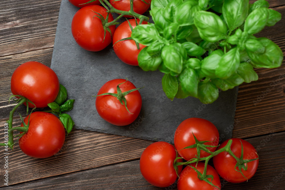 Fresh ripe red tomatoes on a cutting board with fresh basil on a wooden background. Freshly picked red tomatoes and basil leaves for cooking. top view Fresh ripe red tomatoes on a cutting board with fresh basil on a wooden background. Freshly picked red tomatoes and basil leaves for cooking. top view