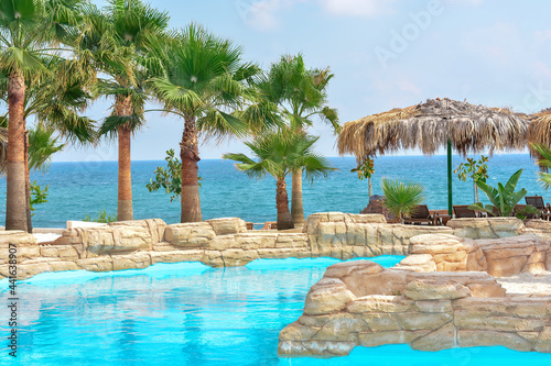 Fototapeta Naklejka Na Ścianę i Meble -  Tropical pool with beautiful palm trees and thatched umbrellas against the backdrop of the sea. Vacation concept, travel. Beautiful landscape