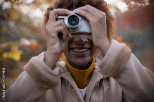 Happy young woman using digital camera in autumn park