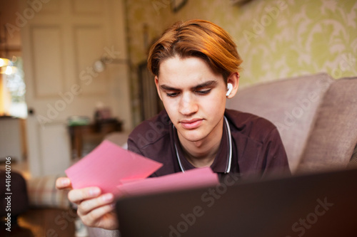 Focused teenage boy studying with flash cards on sofa photo