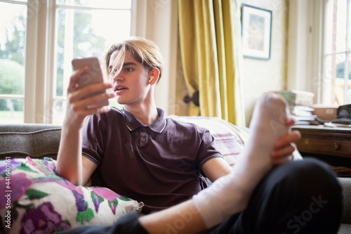 Teenage boy using smart phone at on living room sofa photo