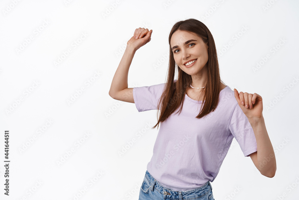 Portrait of beautiful young woman dancing, raising hands up free and relaxed, smiling white teeth, enjoying summer, partying, standing against white background Portrait of beautiful young woman dancing, raising hands up free and relaxed, smiling white teeth, enjoying summer, partying, standing against white background