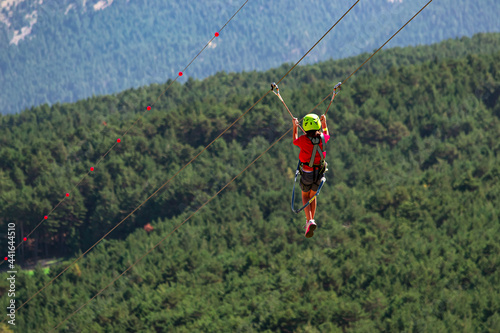 Girl gliding in extreme road trolley zipline in forest on carabiner safety link on tree to tree in Pyrenees of Andorra