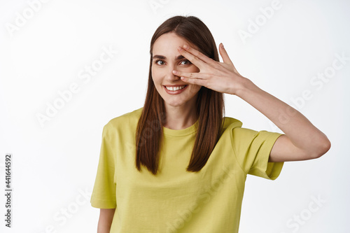 Portrait of smiling girl open her eye, looking happy and friendly, seeing something, standing against white background in yellow t-shirt