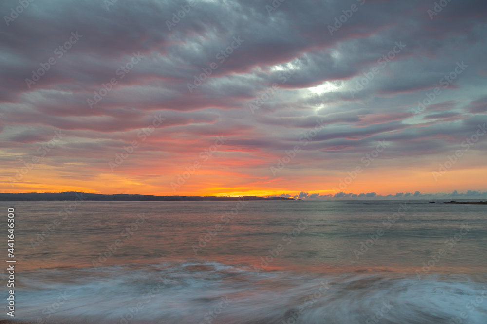 Cloud covered sunrise seascape tinged with pink