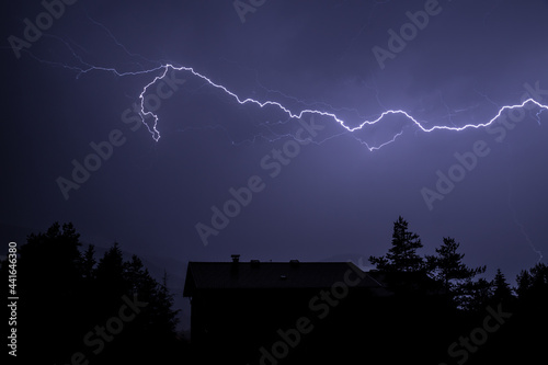 Blitze über einem Haus zwischen Bäumen