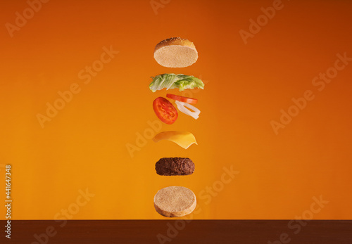 Burger ingredients falling down one by one to create a perfect meal. Colorful conceptual picture of burger cooking.  Orange Background photo