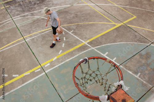 High angle view of a young man bouncing a basketball on an abandoned court.