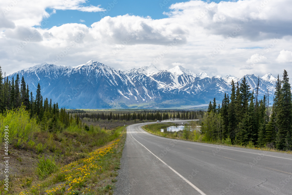 Huge snow capped mountain scene seen outside of Haines Junction, Yukon Territory, Canada with winding road heading to road trip, awe inspriring mountains in spring time. 