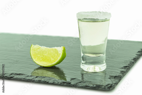 Shot glass with tequila and lime on a white background