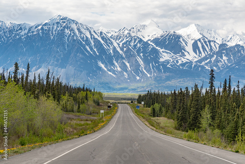 Alaska Highway driving into Haines Junction town in spring time with epic, huge mountains in far distance with amazing scenic drive ahead. Tourists, tourism shot for camping, RV, road trip.  © Scalia Media