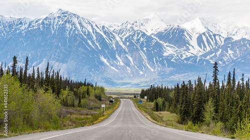 Alaska Highway leading into Haines Junction, Yukon Territory heading north west with massive snow capped mountains in the distance on cloudy, misty morning. 