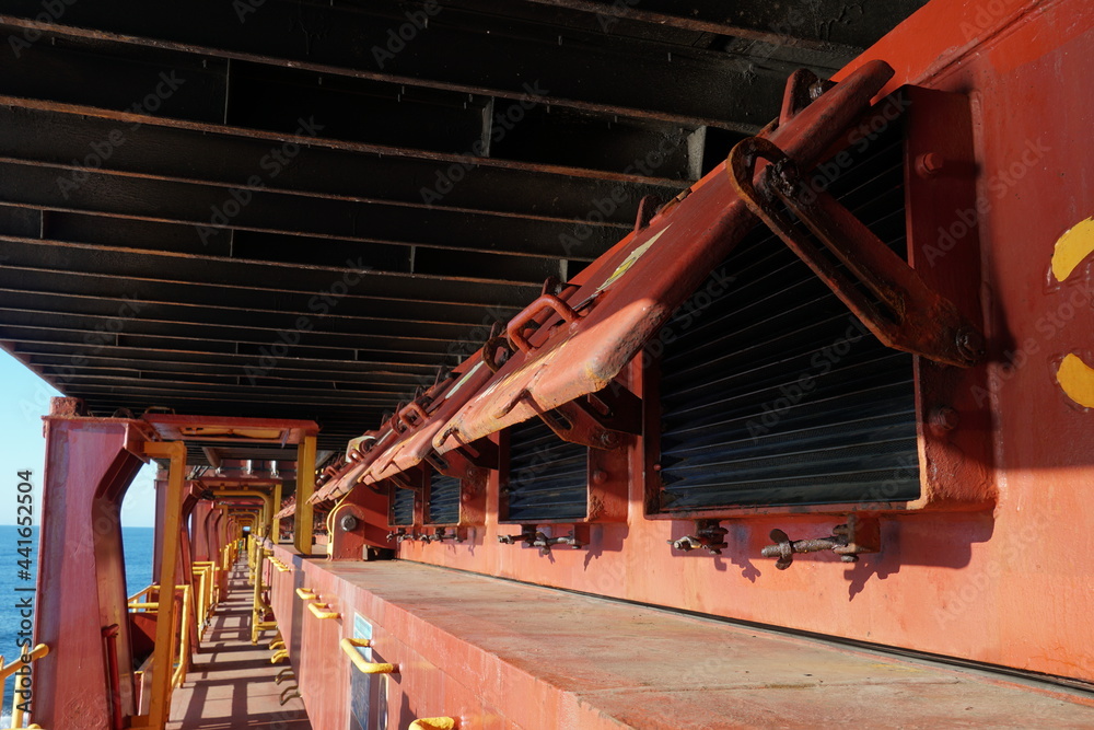 Open ventilation covers in a row of the side of the hatch covers installed on container vessel. Bottom of the container is on the background. Open ventilation covers in a row of the side of the hatch covers installed on container vessel. Bottom of the container is on the background.