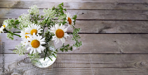 Floral wood background. Banner with a bouquet of daisies in a vase and place for text. Beautiful wildflowers sunny flowers on a wooden background.