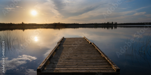Fototapeta Naklejka Na Ścianę i Meble -  Evening sun lights up clouds and an old wooden dock in a calm lake.
