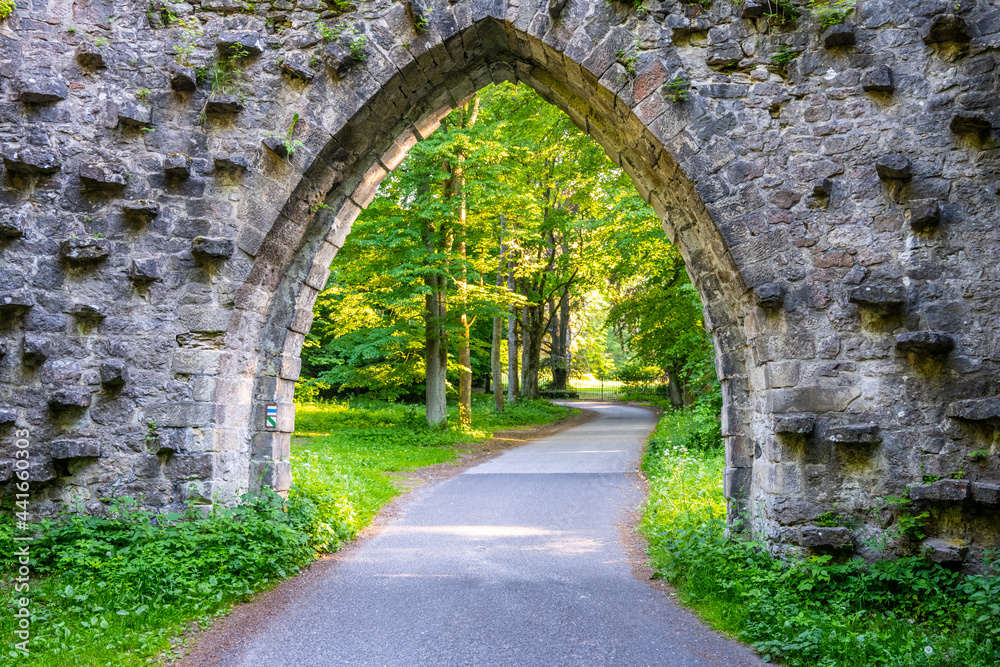 Gothic arc gate over asphalt road in the forest. Arturs Castle near Sychrov, Czech Republic