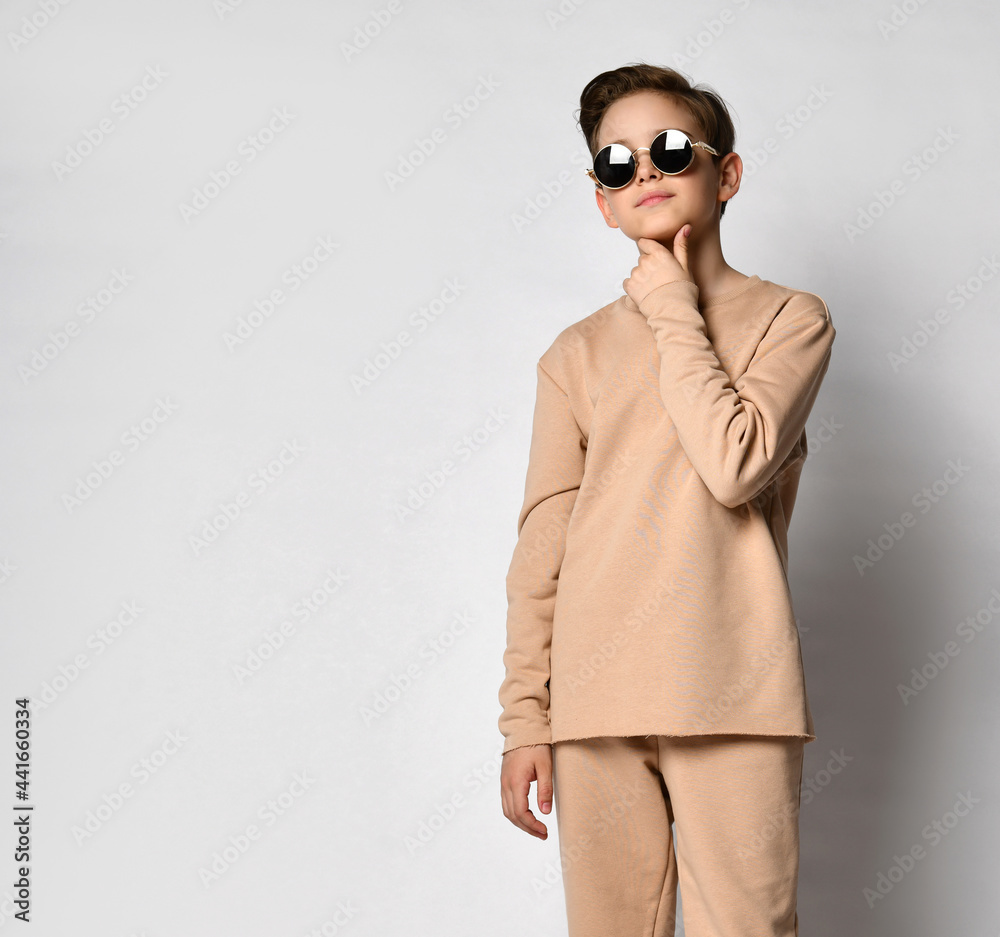 modest guy in a beige Gordian comfortable suit, sweatshirt and tans, stands with his hands folded in front of him, wearing sunglasses. modest guy in a beige Gordian comfortable suit, sweatshirt and tans, stands with his hands folded in front of him, wearing sunglasses.