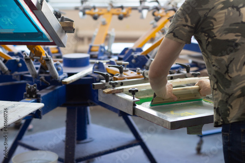 Worker and Serigraphy silk screen print process at clothes factory.